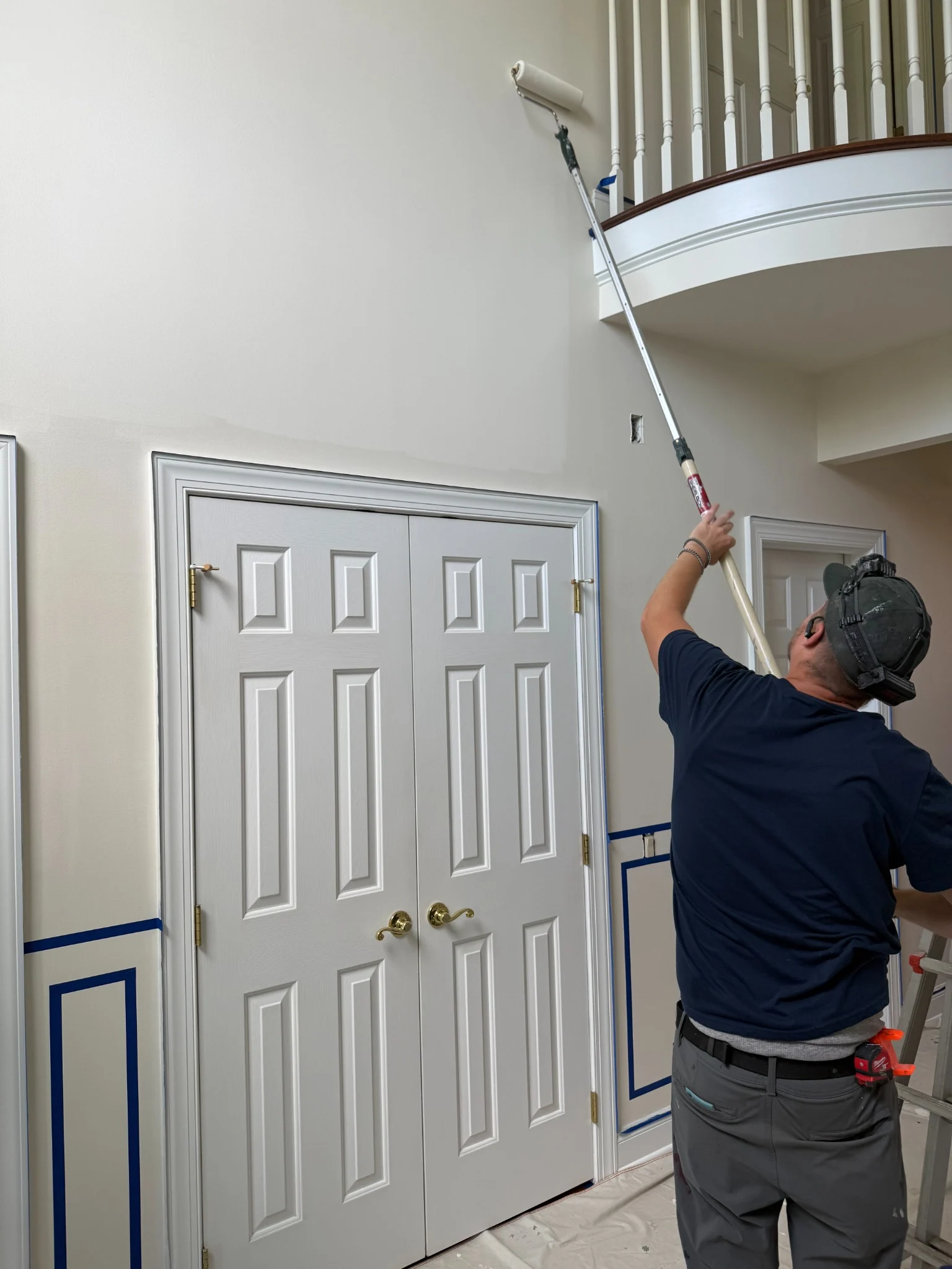 Premier Painting Solutions painter carefully working on a tall interior foyer wall